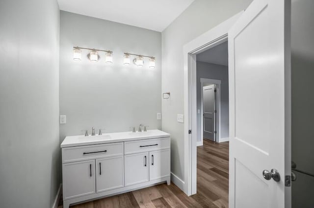 bathroom with double vanity, wood finished floors, a sink, and baseboards