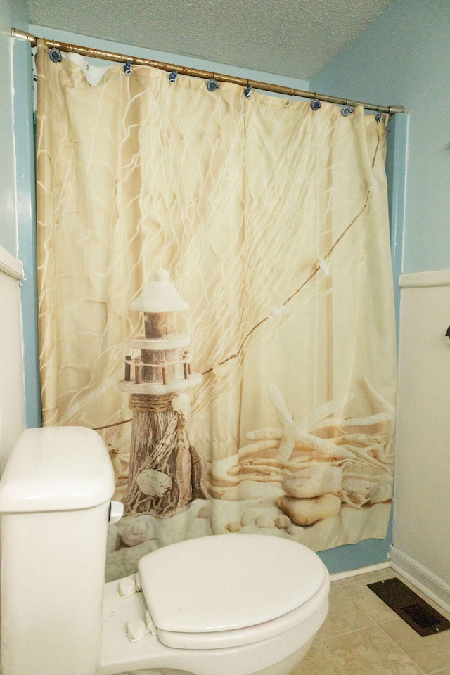 bathroom featuring toilet, a shower with shower curtain, a textured ceiling, and tile patterned floors