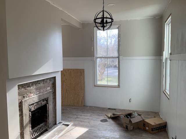 unfurnished living room with a stone fireplace, a healthy amount of sunlight, hardwood / wood-style floors, and an inviting chandelier