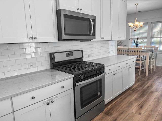 kitchen with white cabinets, dark wood finished floors, light stone countertops, stainless steel appliances, and pendant lighting