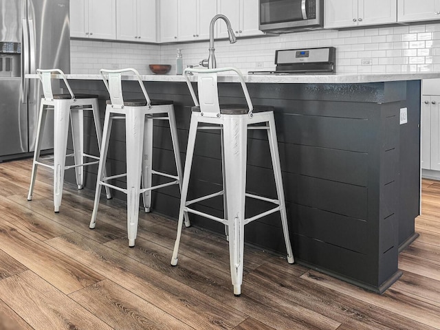 interior details with a breakfast bar, white cabinetry, stainless steel appliances, and dark wood-type flooring