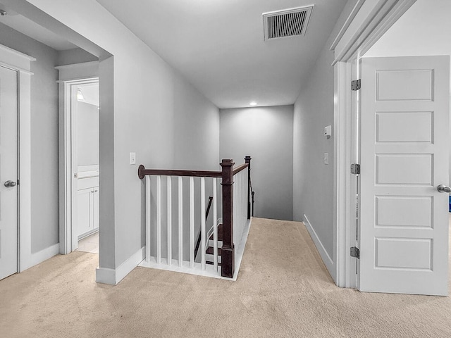 hallway with baseboards, visible vents, light carpet, and an upstairs landing