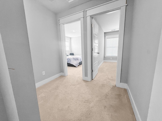 hallway with baseboards and light colored carpet