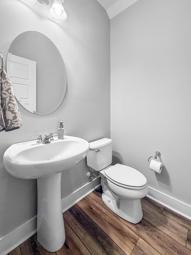 half bath featuring a sink, toilet, baseboards, and wood finished floors