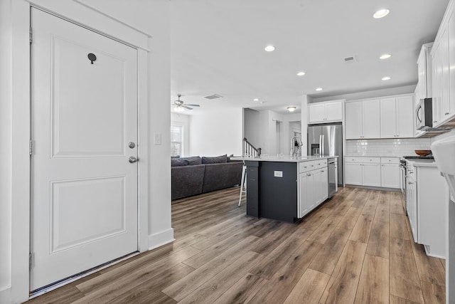 kitchen with open floor plan, light countertops, a center island with sink, and white cabinetry