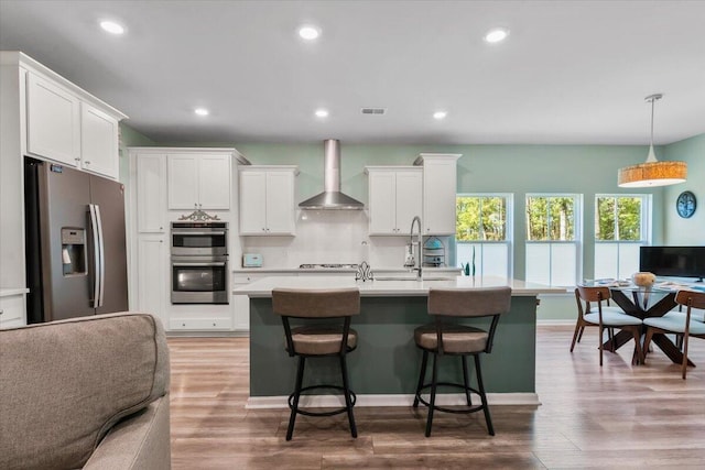 kitchen featuring wall chimney exhaust hood, white cabinetry, appliances with stainless steel finishes, and hardwood / wood-style floors