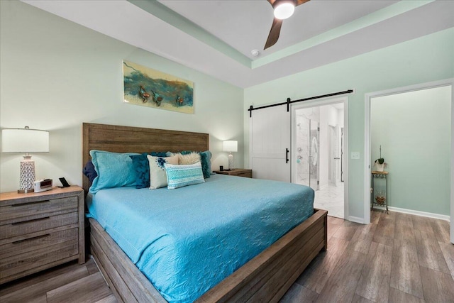 bedroom with ceiling fan, hardwood / wood-style flooring, ensuite bathroom, and a barn door