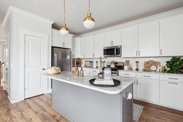 kitchen featuring stainless steel appliances, a center island with sink, pendant lighting, and white cabinetry