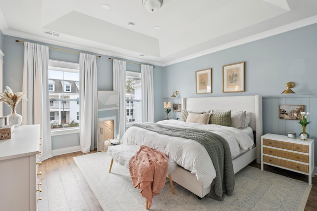 bedroom with a raised ceiling, ornamental molding, and light hardwood / wood-style flooring