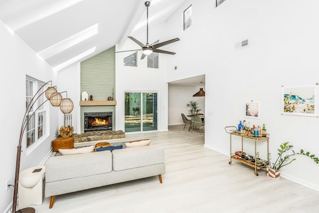 living room with a large fireplace, light hardwood / wood-style floors, high vaulted ceiling, and ceiling fan