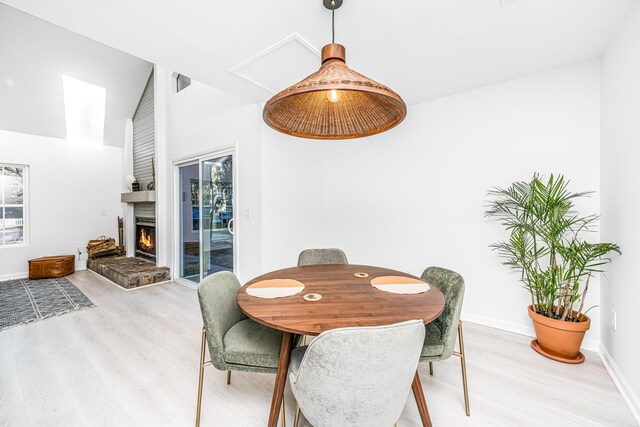 dining space featuring light hardwood / wood-style floors, a fireplace, and high vaulted ceiling