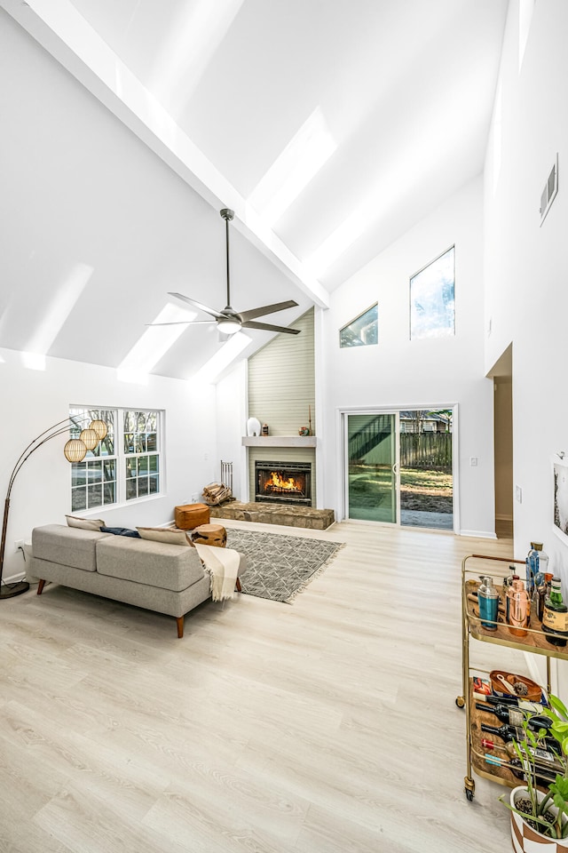 living room with beam ceiling, ceiling fan, high vaulted ceiling, light hardwood / wood-style floors, and a fireplace