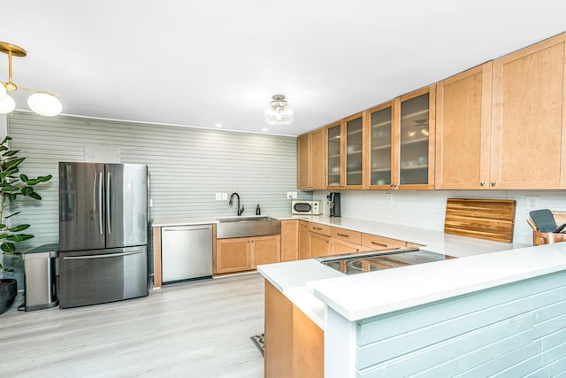 kitchen with kitchen peninsula, appliances with stainless steel finishes, sink, decorative light fixtures, and light hardwood / wood-style flooring