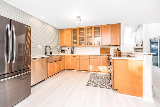 kitchen with sink, kitchen peninsula, wood walls, appliances with stainless steel finishes, and light wood-type flooring