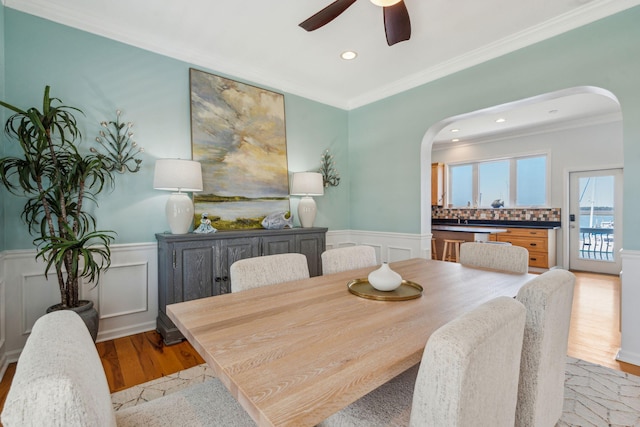 68 W 9th St Unit B, Folly Beach, SC 29439 - dining room with a wainscoted wall, a ceiling fan, arched walkways, crown molding, and light wood-style flooring