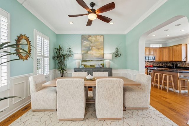 68 W 9th St Unit B, Folly Beach, SC 29439 - dining room featuring a wainscoted wall, a ceiling fan, arched walkways, crown molding, and light wood-style flooring