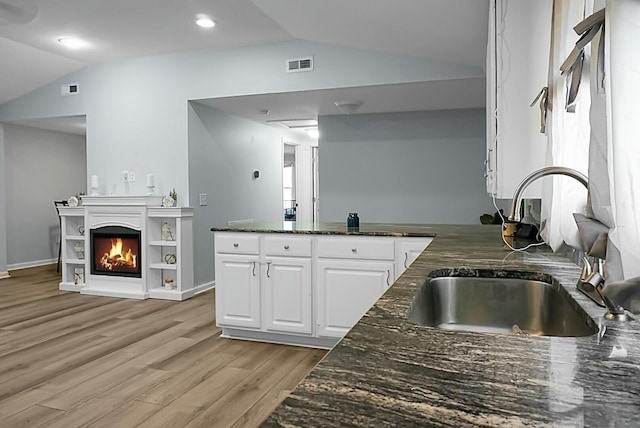 kitchen with light hardwood / wood-style floors, white cabinets, dark stone countertops, sink, and lofted ceiling