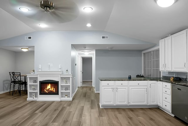 kitchen featuring stainless steel dishwasher, light hardwood / wood-style flooring, vaulted ceiling, white cabinetry, and dark stone counters