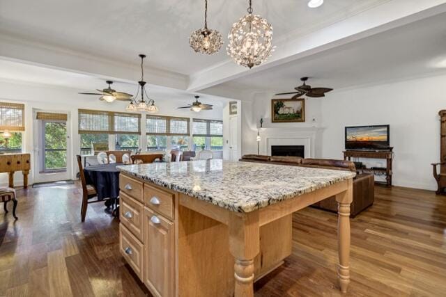 kitchen featuring dark wood-type flooring, a center island, hanging light fixtures, beam ceiling, and light stone countertops