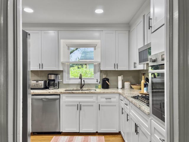 kitchen featuring stainless steel appliances, white cabinetry, a sink, and light stone counters