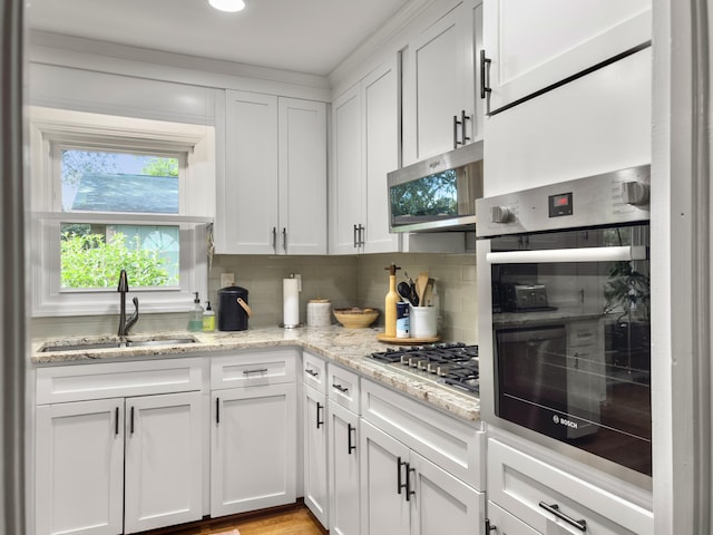 kitchen featuring light stone counters, stainless steel appliances, a sink, white cabinets, and tasteful backsplash