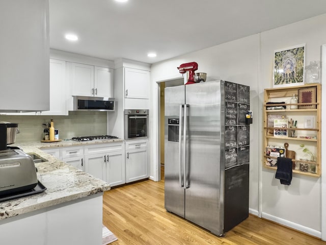 kitchen featuring light wood-style flooring, appliances with stainless steel finishes, white cabinets, and light stone counters