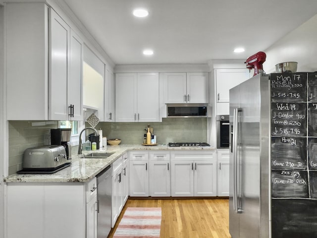 kitchen featuring appliances with stainless steel finishes, light stone counters, light wood-type flooring, white cabinetry, and a sink