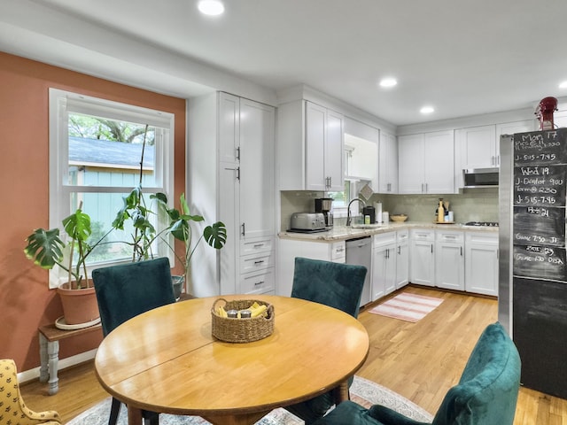 kitchen with light wood-type flooring, tasteful backsplash, appliances with stainless steel finishes, and white cabinetry