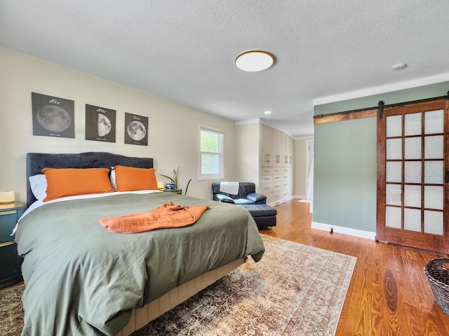 bedroom featuring baseboards, a barn door, a textured ceiling, and light wood-style floors