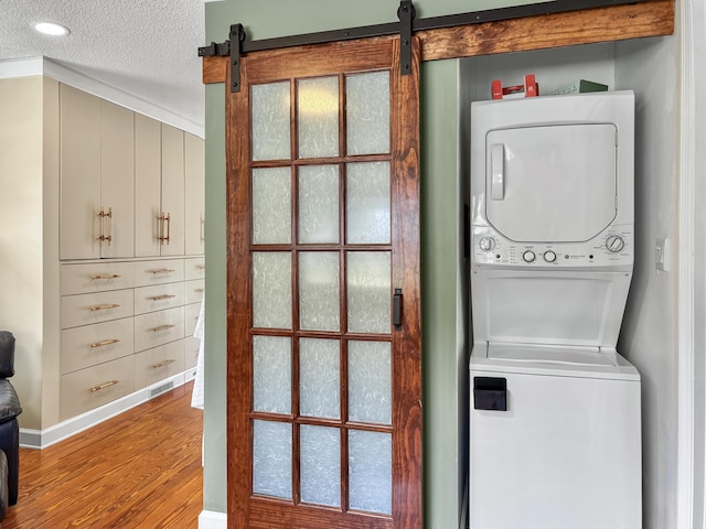 clothes washing area featuring a textured ceiling, stacked washer and dryer, a barn door, and wood finished floors