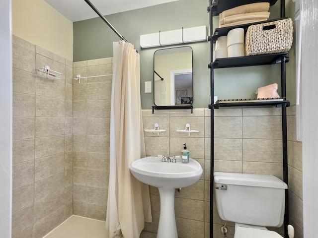 bathroom with a tile shower, toilet, and tile walls