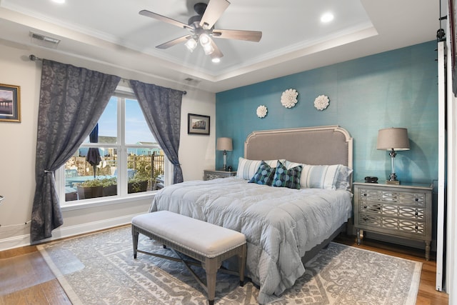 bedroom featuring crown molding, hardwood / wood-style floors, and a tray ceiling