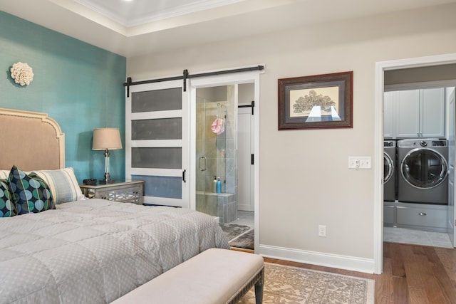 bedroom featuring wood-type flooring, a barn door, separate washer and dryer, and crown molding