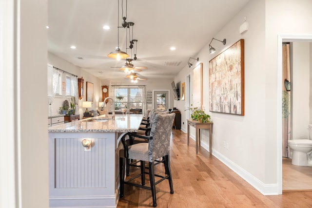 kitchen featuring a breakfast bar, decorative light fixtures, sink, light hardwood / wood-style floors, and light stone countertops