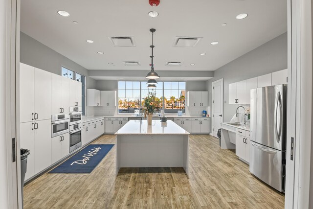 kitchen with pendant lighting, stainless steel appliances, a center island, light hardwood / wood-style floors, and white cabinets