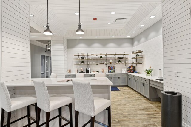 bar with hanging light fixtures, gray cabinets, and light wood-type flooring