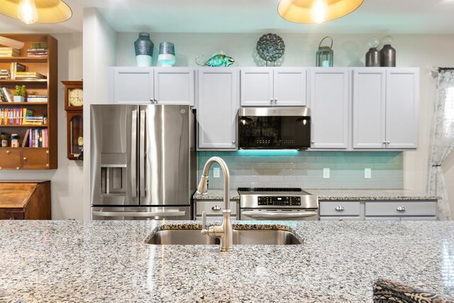 kitchen with stainless steel appliances, white cabinetry, sink, and light stone counters