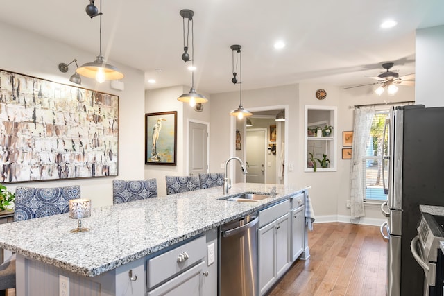 kitchen featuring sink, a kitchen island with sink, hanging light fixtures, stainless steel appliances, and light stone countertops