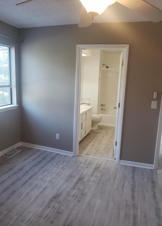 unfurnished bedroom featuring a textured ceiling, connected bathroom, light hardwood / wood-style floors, and ceiling fan