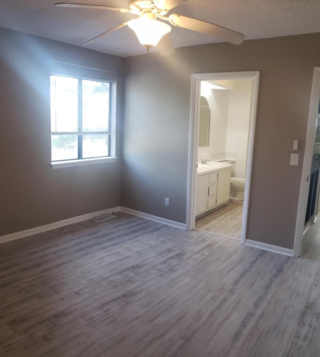 unfurnished bedroom featuring connected bathroom, ceiling fan, a textured ceiling, and light wood-type flooring