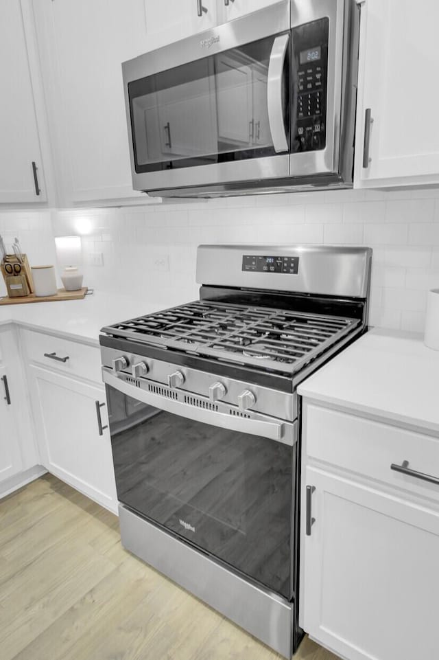 kitchen featuring white cabinetry, appliances with stainless steel finishes, backsplash, and light wood-type flooring