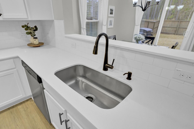 room details with dishwasher, sink, white cabinets, decorative backsplash, and light hardwood / wood-style flooring