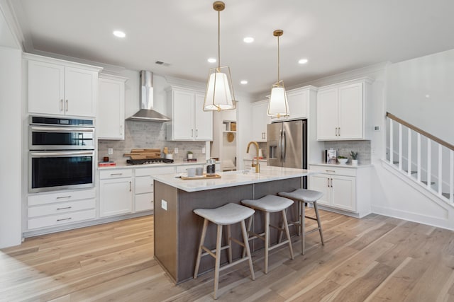 kitchen with appliances with stainless steel finishes, a breakfast bar, white cabinets, and wall chimney range hood