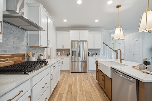 kitchen featuring a sink, stainless steel appliances, white cabinets, and wall chimney range hood