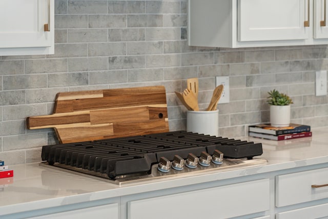 room details with white cabinetry, decorative backsplash, stainless steel gas stovetop, and light countertops