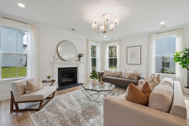 living area with a notable chandelier, a fireplace with flush hearth, visible vents, and light wood-type flooring