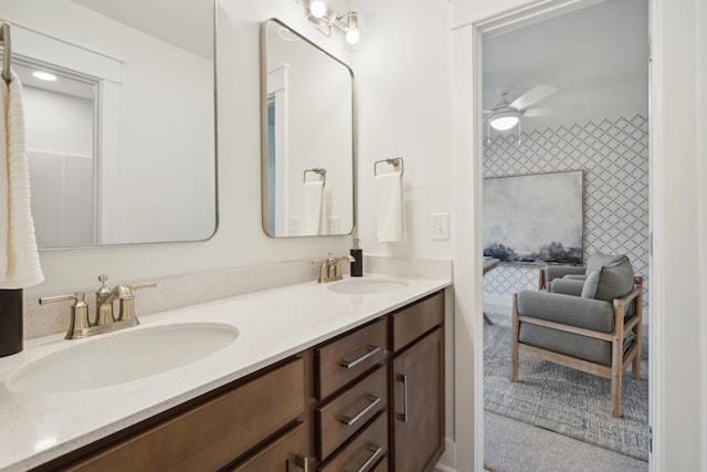 bathroom featuring ceiling fan, double vanity, wallpapered walls, and a sink