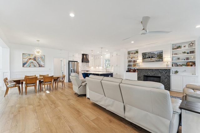 living room featuring built in features, light hardwood / wood-style flooring, a tile fireplace, and ceiling fan