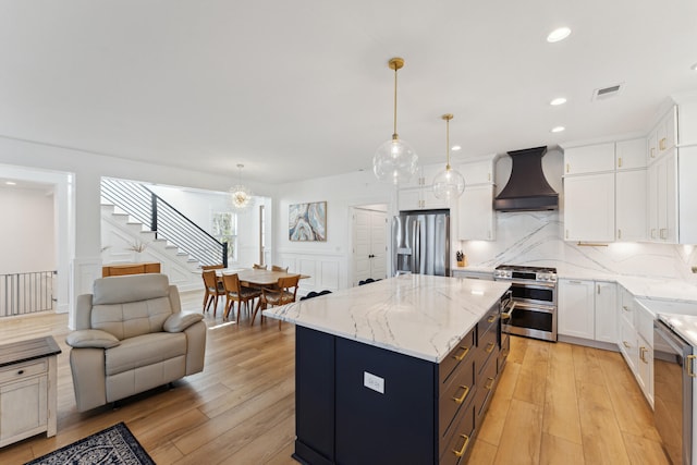 kitchen with premium range hood, appliances with stainless steel finishes, decorative light fixtures, and a kitchen island