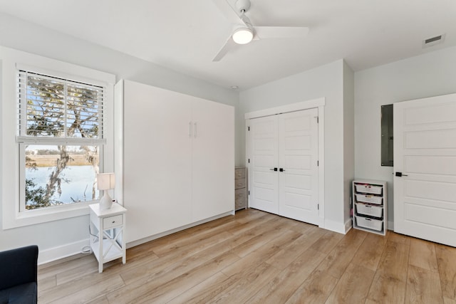 unfurnished bedroom featuring ceiling fan, electric panel, light wood-type flooring, and a closet